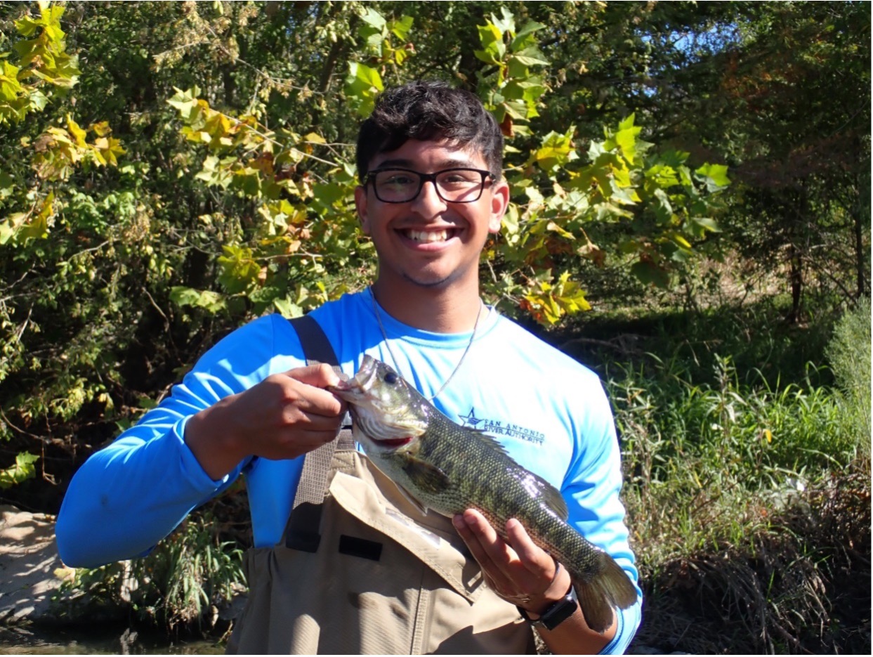 A young man holds a Guadalupe bass in his hands.