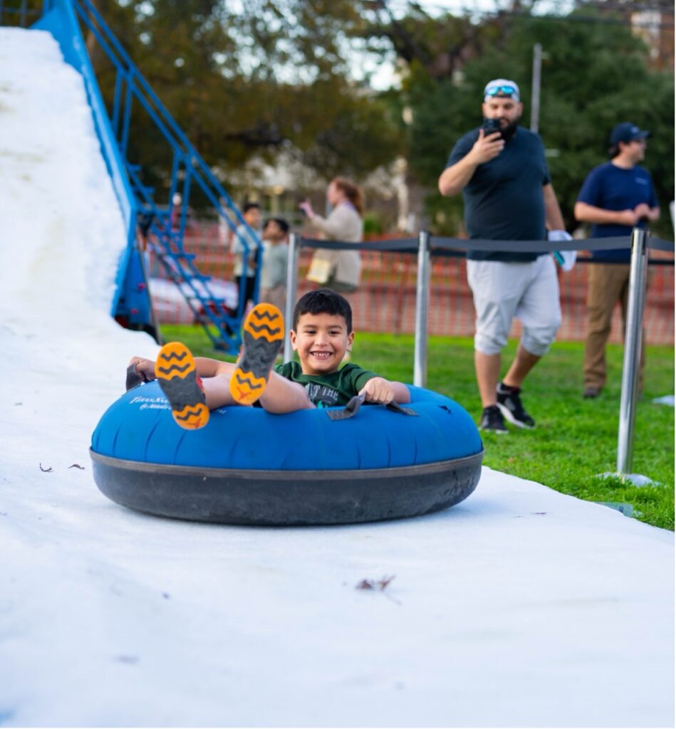 A child slides down a path of snow in an inner tube at River of Lights event.