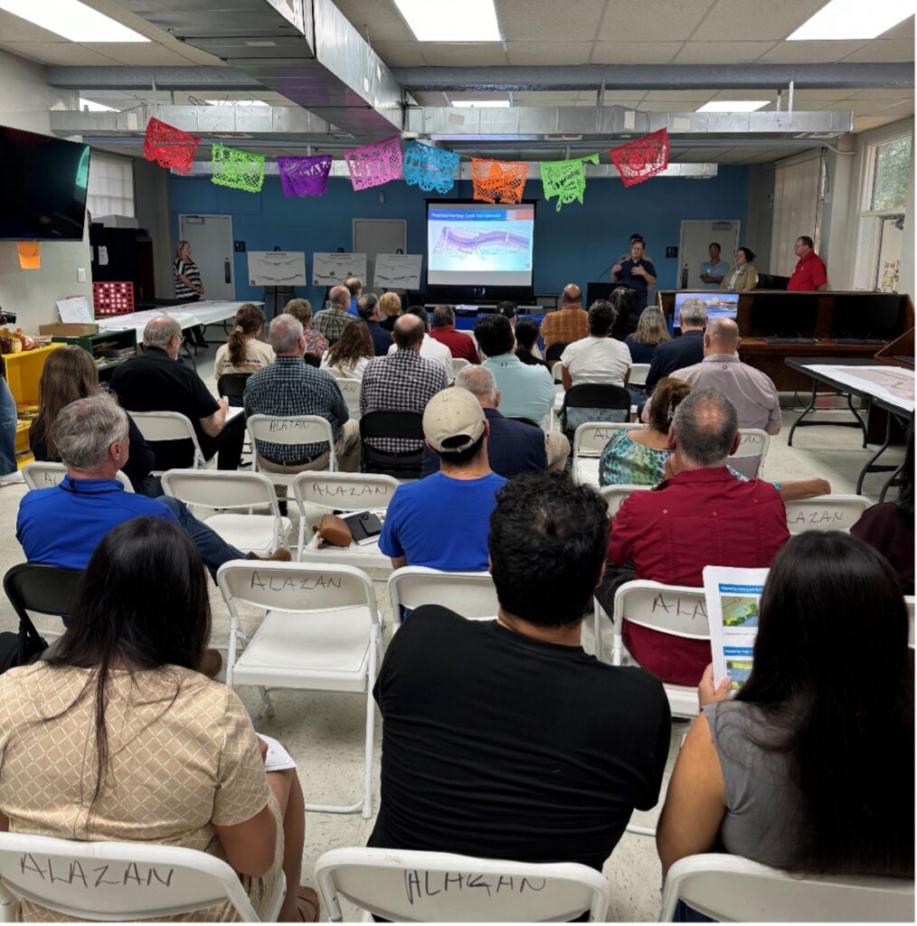 A room filled with people facing a presentation screen during the Westside Creeks Ecosystem Restoration Project