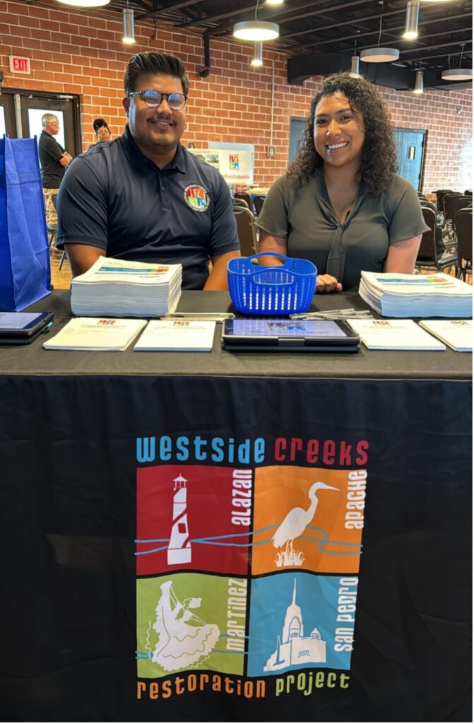 A man and woman sit behind the checkin table at the Westside Creeks Ecosystem Restoration Meetings