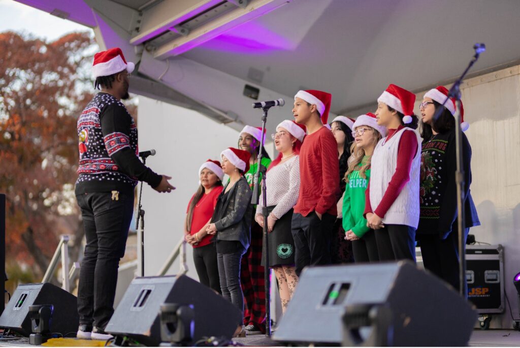 A choir of children sing on stage dressed in festive Christmas wear.