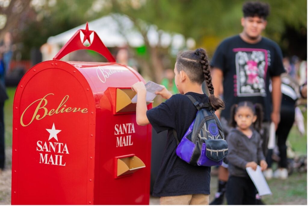 A child places a letter into a large mailbox intended for Santa Claus. 