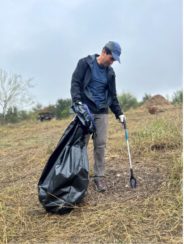 A man uses trash grabber to pick up trash in a field.